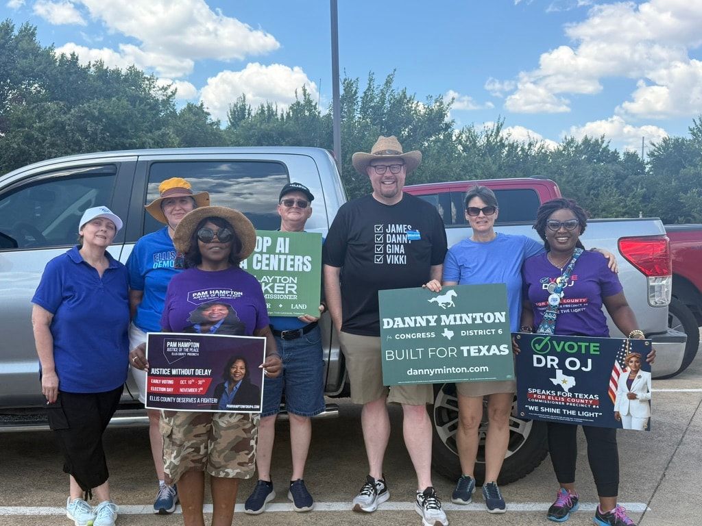 Eight volunteers in sun hats and campaign shirts standing in a car park on a hot day, holding Danny Minton for Congress and other campaign signs