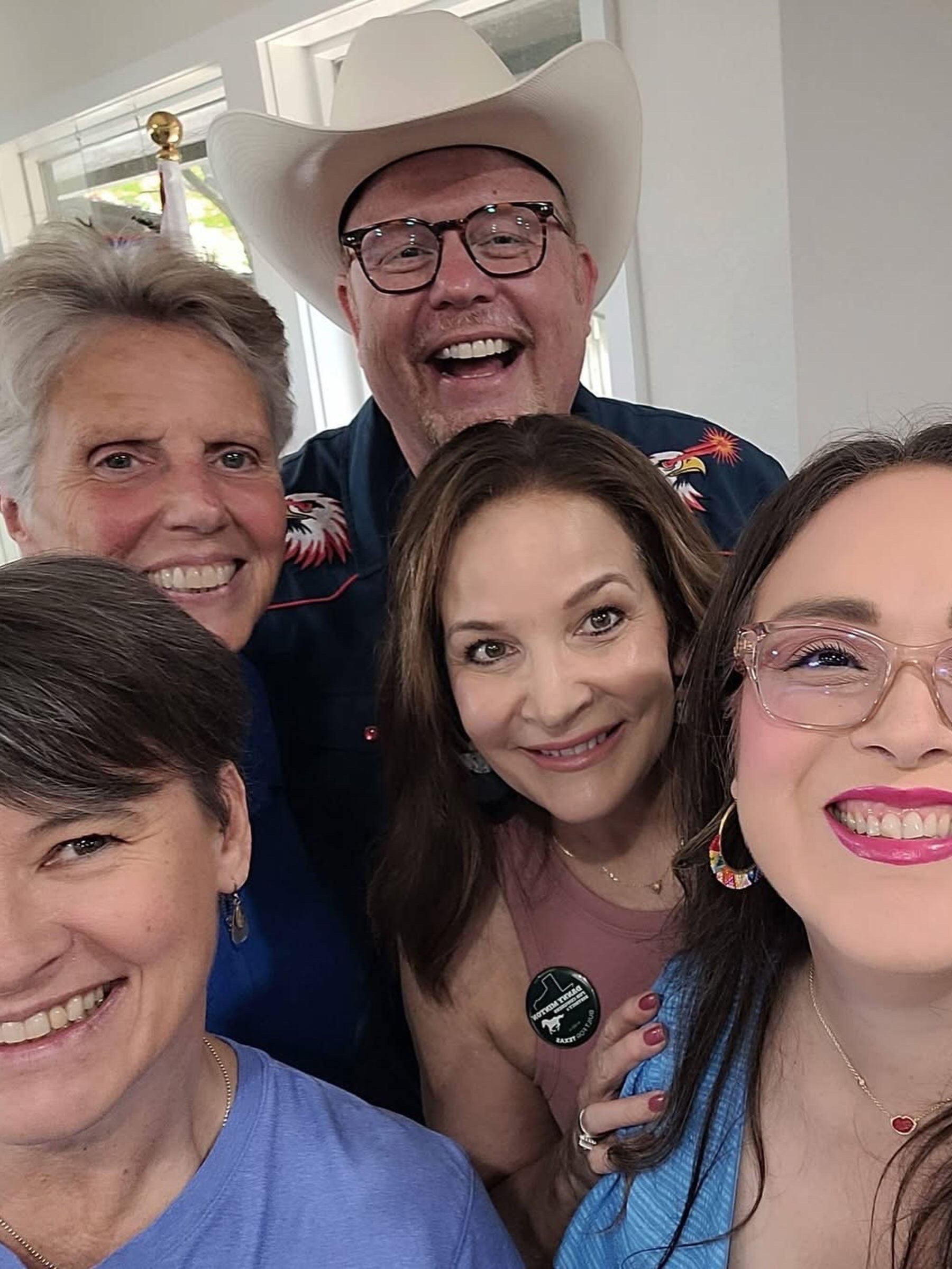 A close-up group selfie of five smiling supporters, one of them in a white cowboy hat