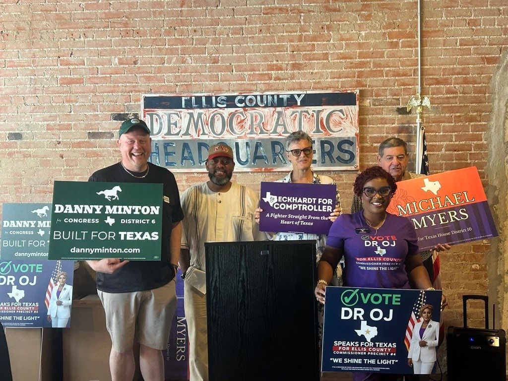 Supporters standing with campaign signs in front of a hand-painted Ellis County Democratic Headquarters banner