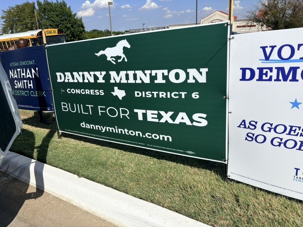 A large green campaign banner reading Danny Minton for Congress, District 6, Built for Texas, standing beside other candidates' signs