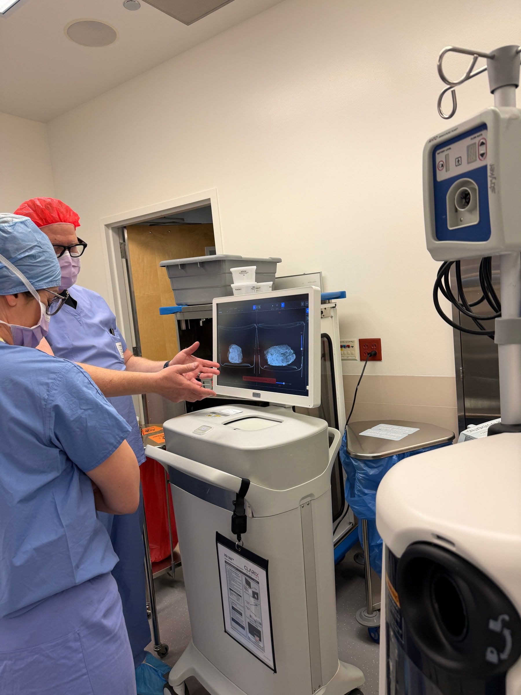 Danny Minton in surgical scrubs in an operating room, reviewing an imaging screen